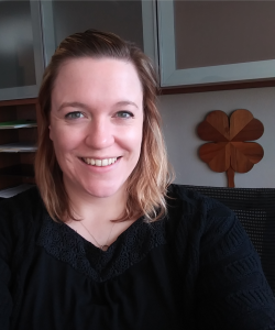 Emily Crook, Positive Youth Development Educator in her office with a wooden four leaved clover behind her left shoulder. 