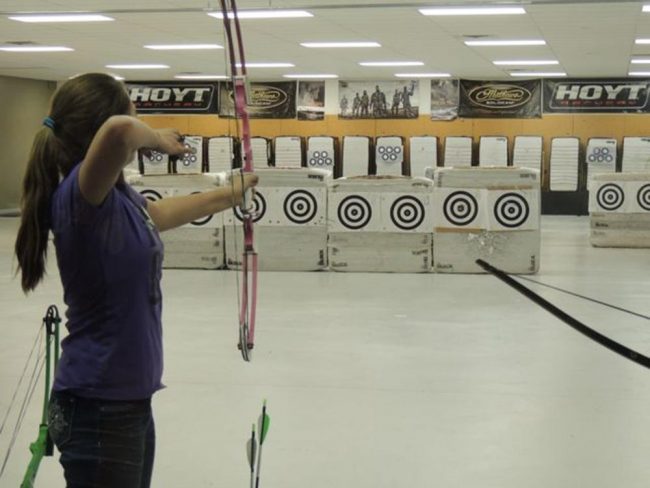 youth aiming arrow and bow at a row of targets