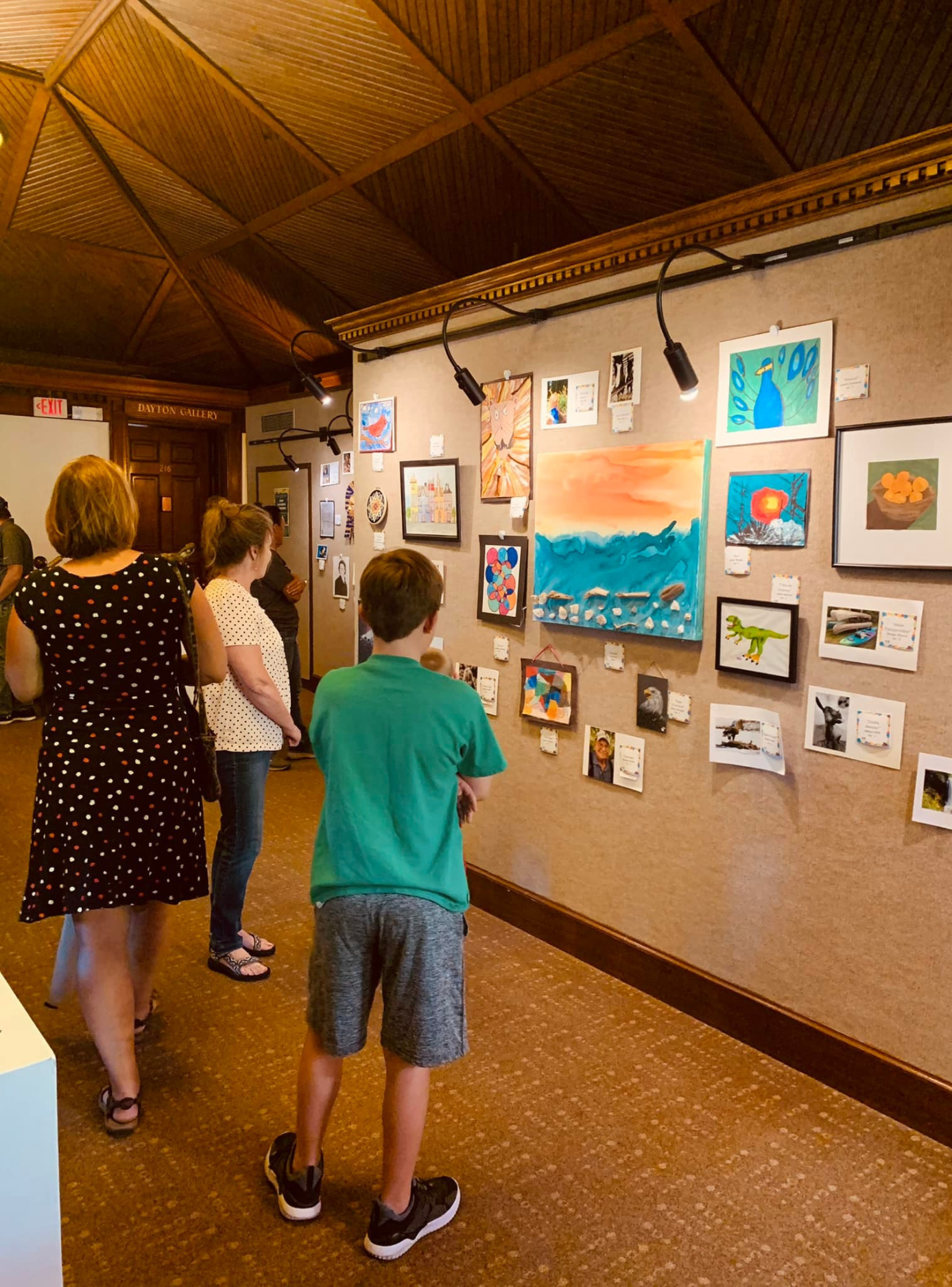 Pump House visitors gazing at 4-H art on a gray wall. 