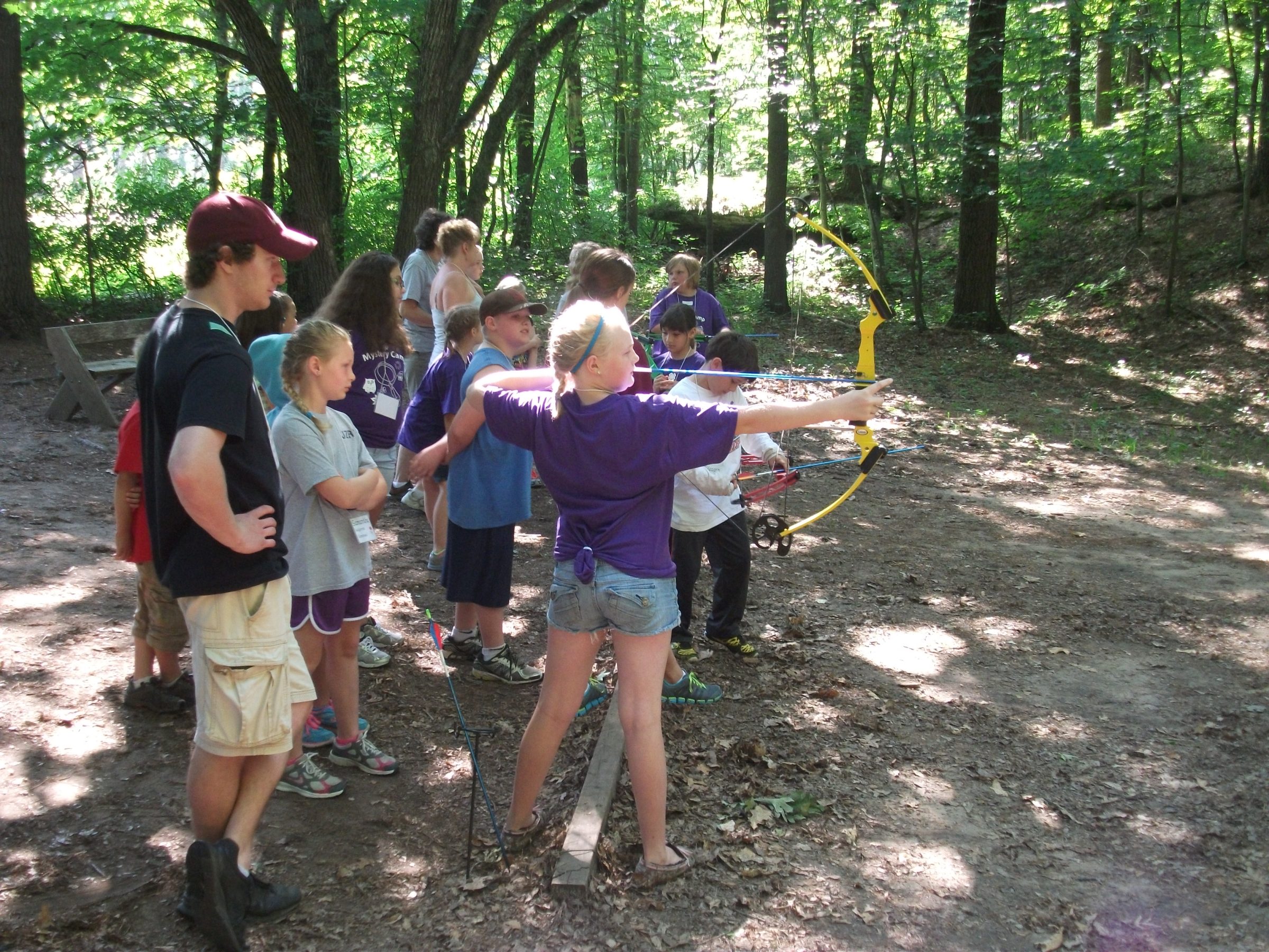 Youth lining up in a forest to shoot arrows